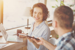 Jeune femme souriante sur son ordinateur portable, récupérant une tablette tendue par un homme
