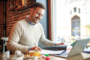 un homme heureux prenant des notes manuscrites avec son ordinateur portable devant lui