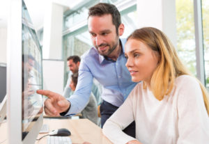 Jeune femme suivant une formation devant un ordinateur, conseillée par son formateur.