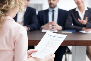 Une femme de dos tenant son CV, assise face à 3 personnes